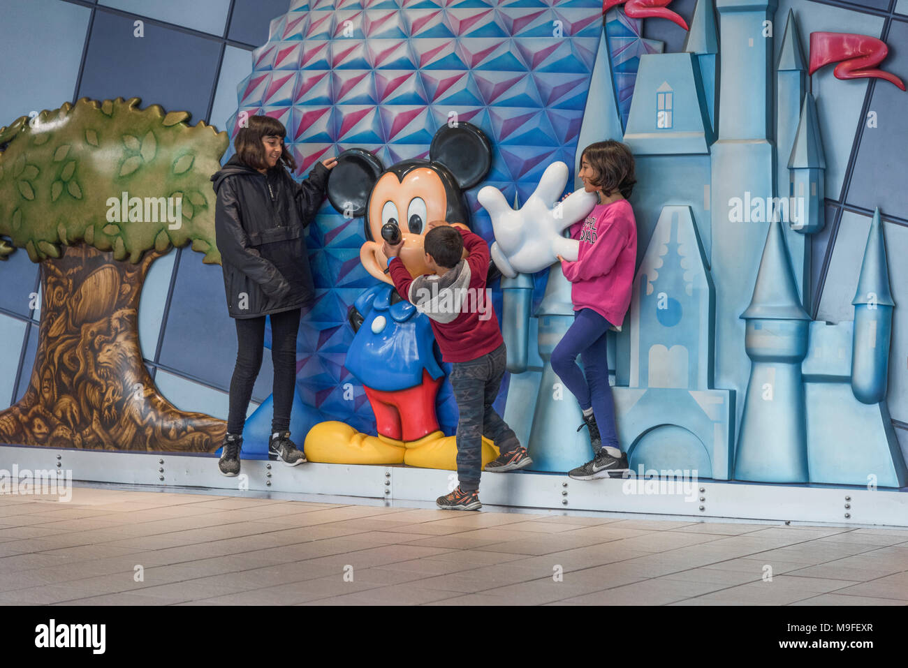 Les enfants posant avec un Micky Mouse statue situé dans l'aérogare à l'Aéroport International d'Orlando en Floride USA. Banque D'Images
