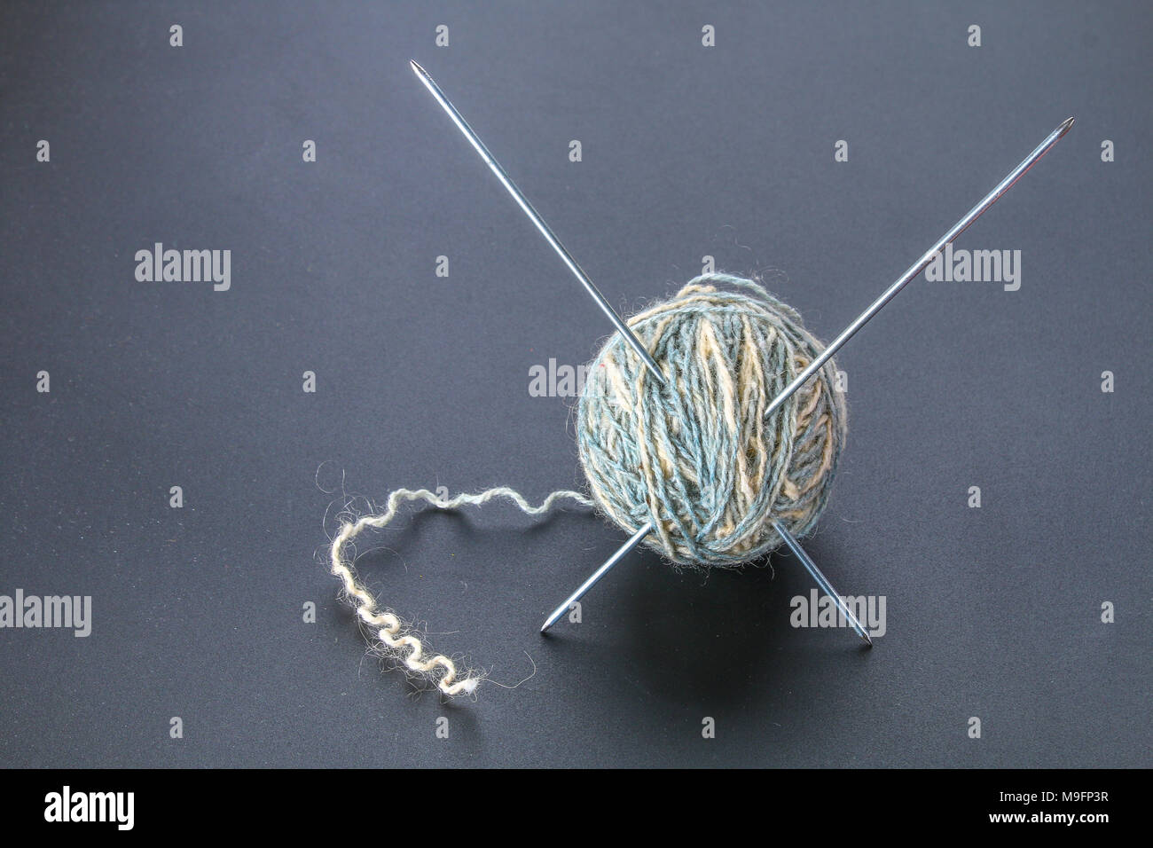Une balle de laine avec des aiguilles à tricoter et de chaussettes sur un tableau gris. La couture Banque D'Images