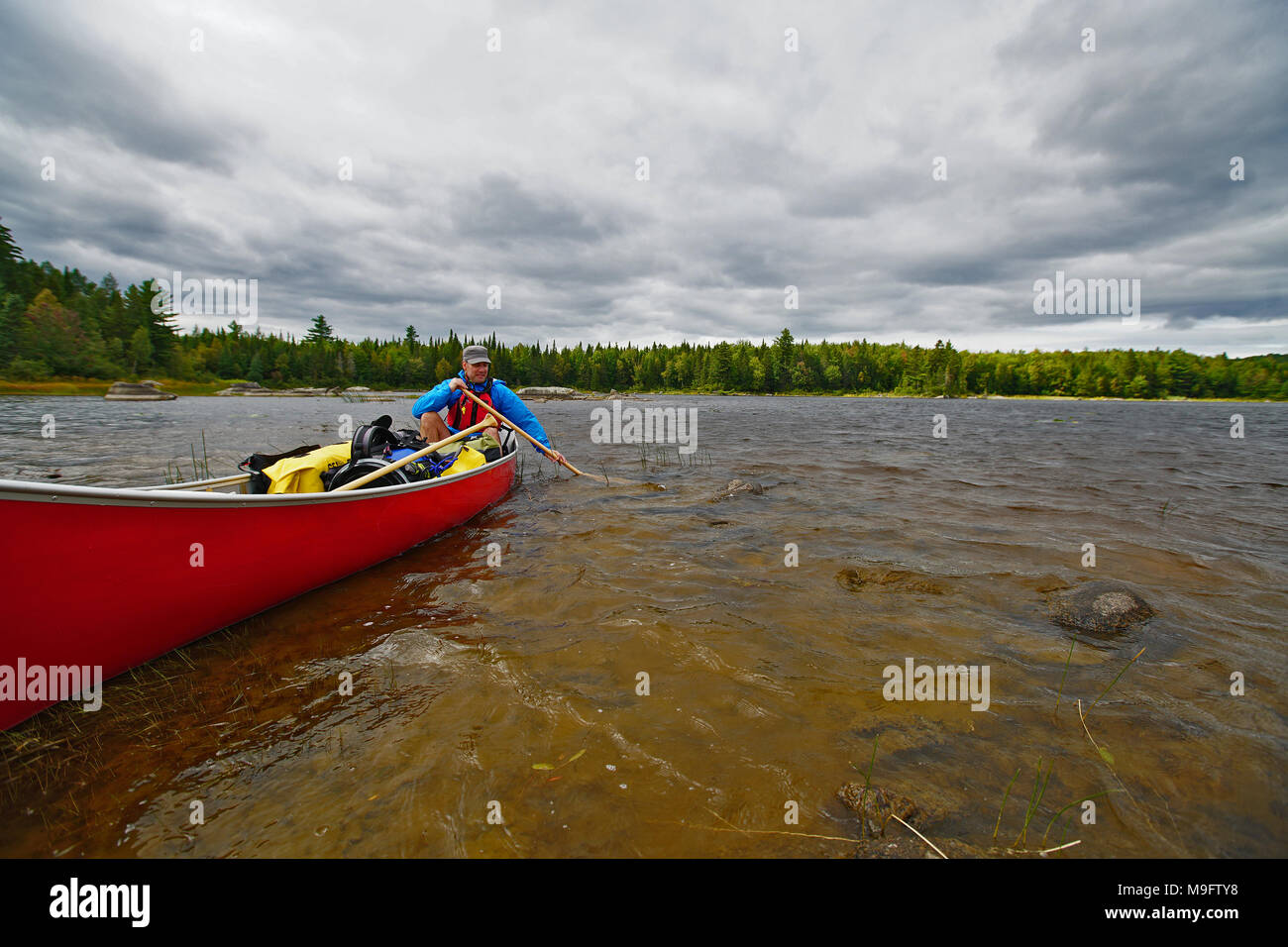 Homme dans un canot à terre rouge de l'aviron dans un lac avec des skis nuageux saccadée Banque D'Images