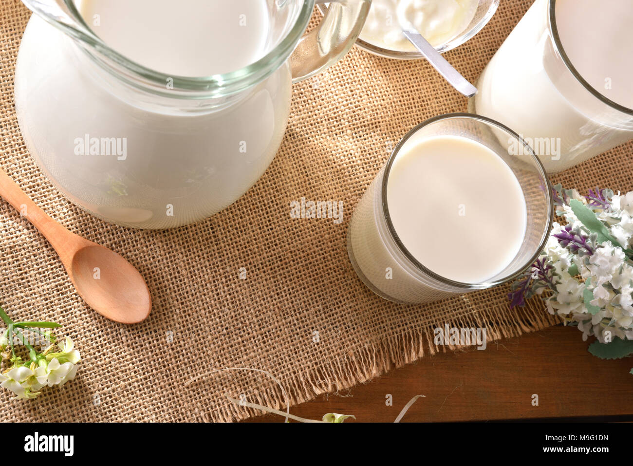 Le lait contenant sur nappe de toile avec fleurs décoratives piscine dans la nature. Composition horizontale. Banque D'Images