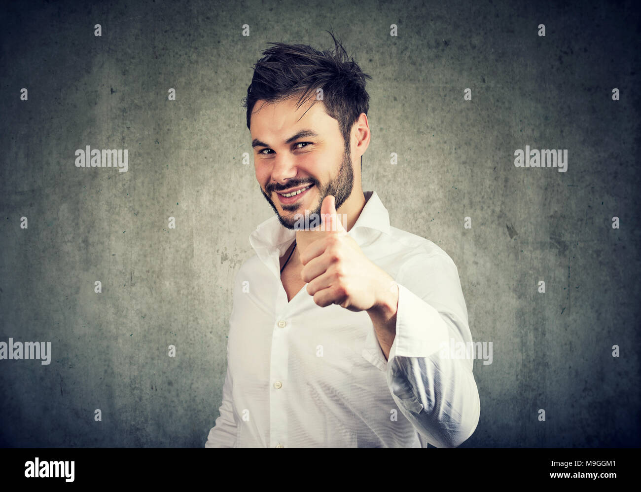 Succès de jeune homme en chemise blanche en donnant comme et showing thumb up avec sourire. Banque D'Images
