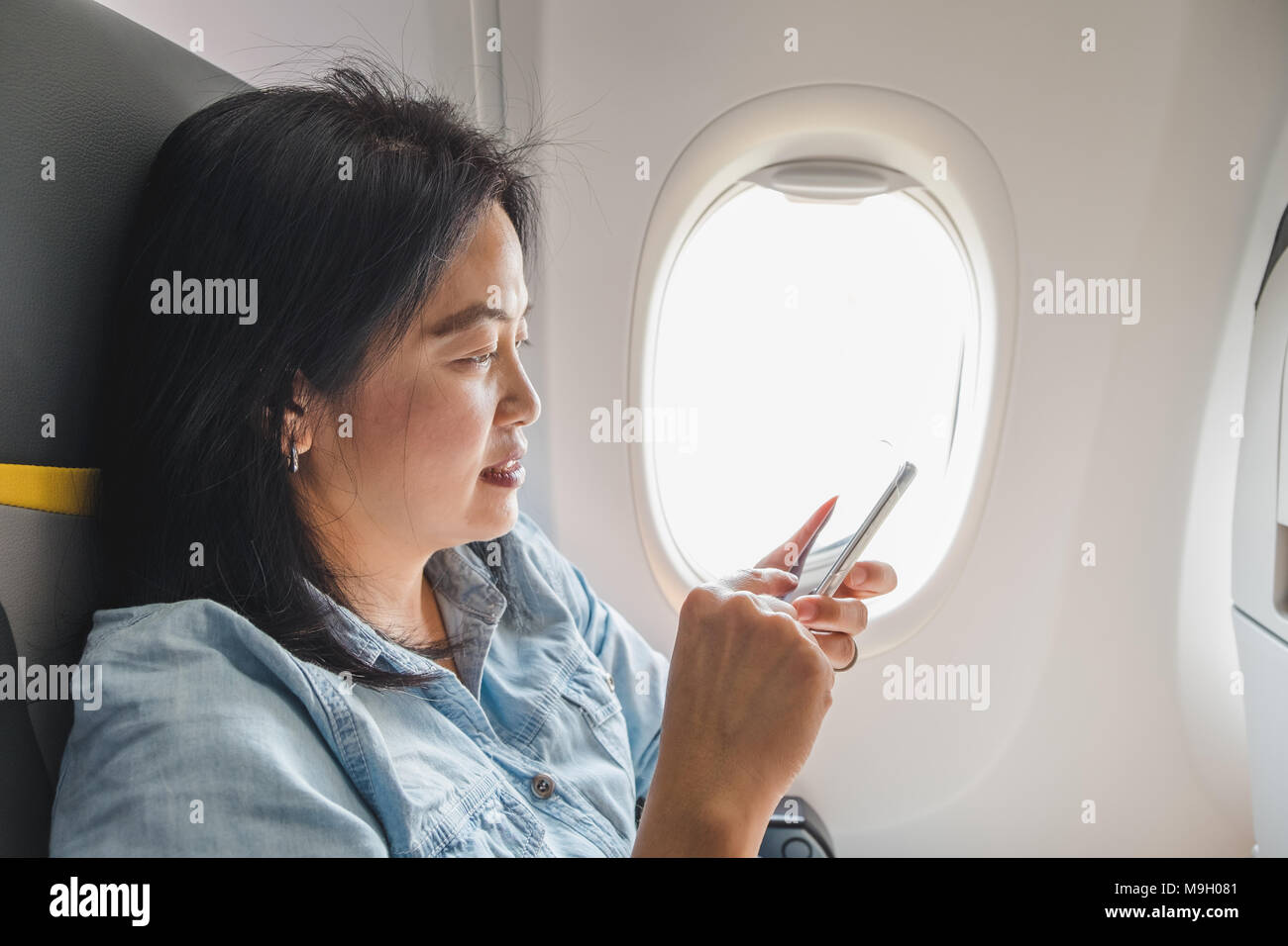 Asian Woman sitting at hublot dans l'avion et activez le mode Avion sur téléphone mobile avant de décoller. Banque D'Images