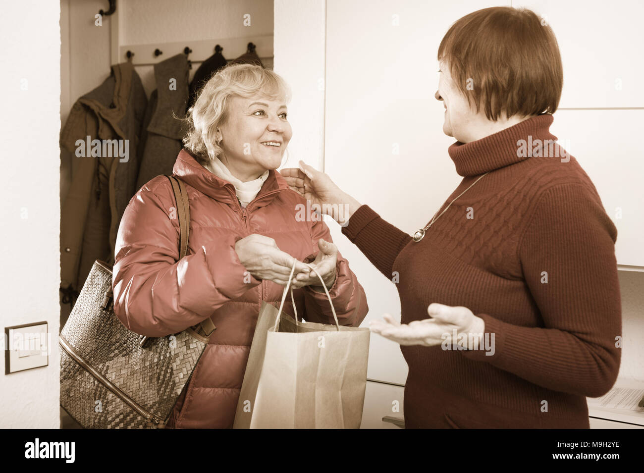 Vieille Femme positive de dire au revoir à un ami femme en veste à l'intérieur Banque D'Images
