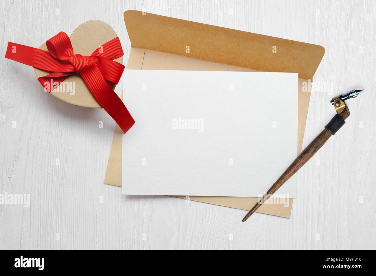 Plume calligraphique maquette une enveloppe avec une lettre et un cadeau avec un arc rouge, carte de souhaits pour la Saint-Valentin avec place pour votre texte. Mise à plat, haut voir photo maquette Banque D'Images