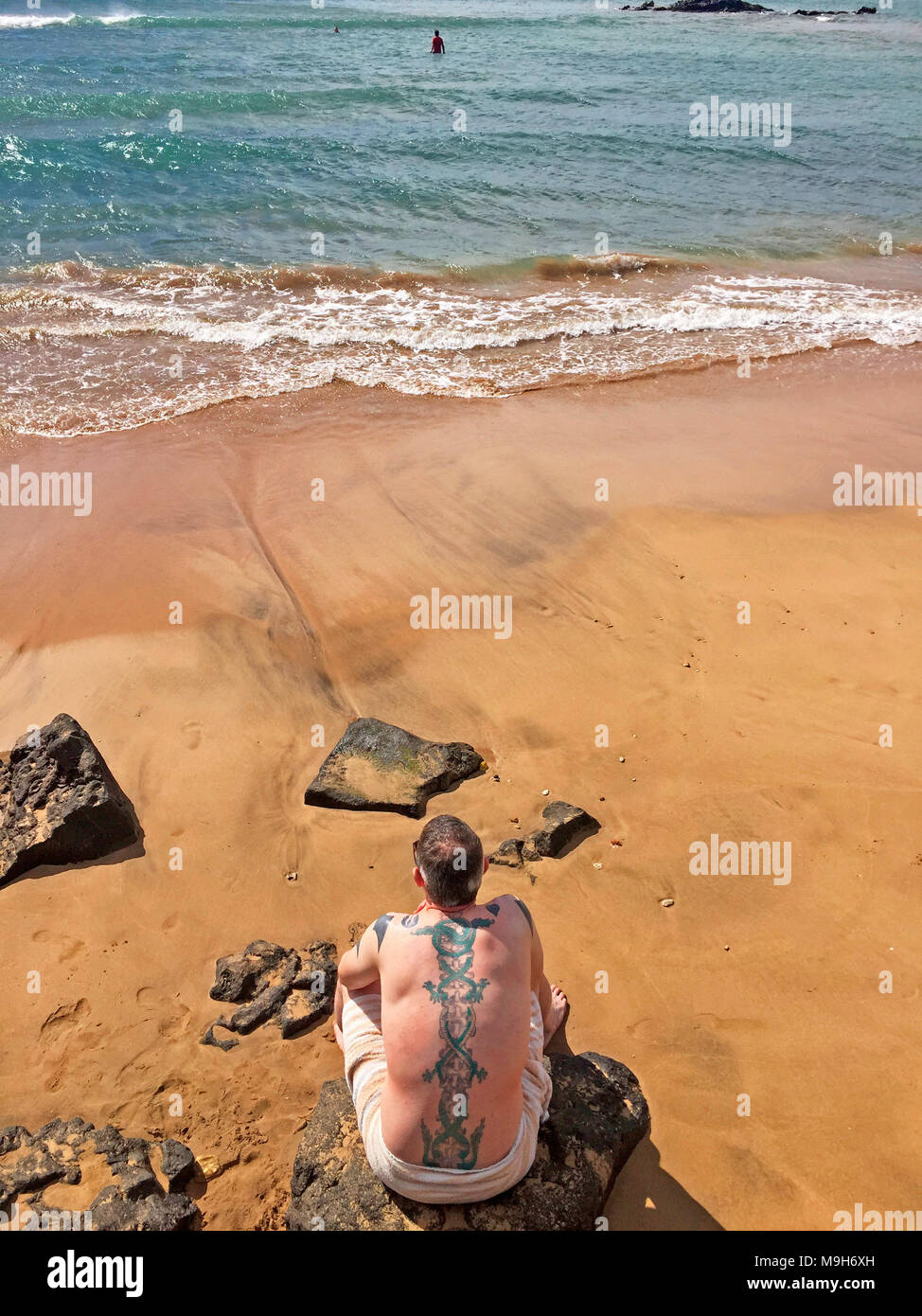 Un homme avec des tatouages visibles sur le dos et les bras de l'action vue sur l'eau de la plage, Maui, États-Unis Banque D'Images