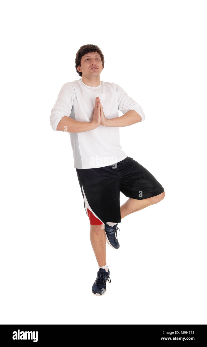 Un jeune homme séduisant en shorts et T-short debout sur une jambe avec les mains pliées, méditant, isolée pour fond blanc Banque D'Images