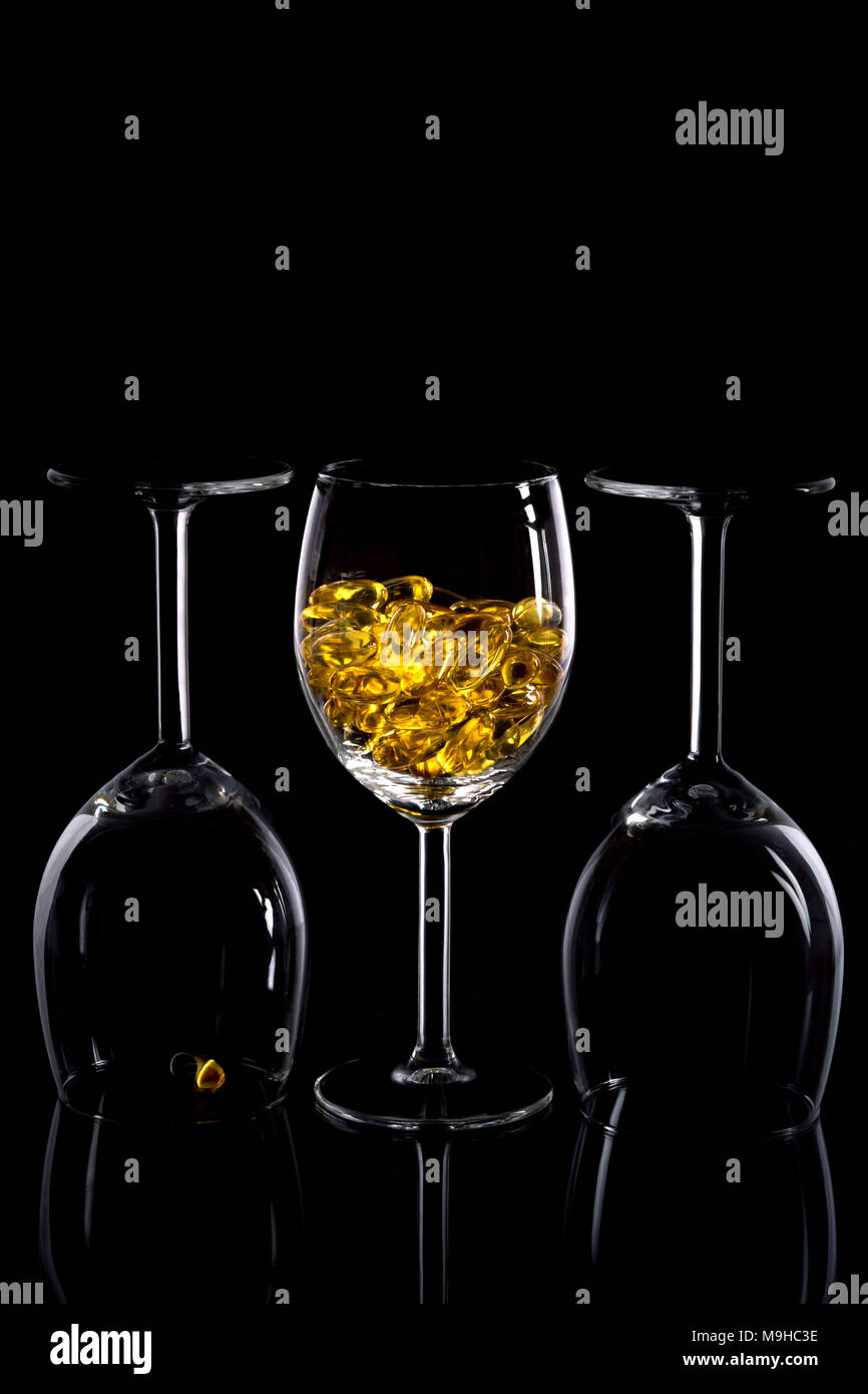 Trois verres à vin avec des pilules jaunes contre un arrière-plan noir élégant. Banque D'Images