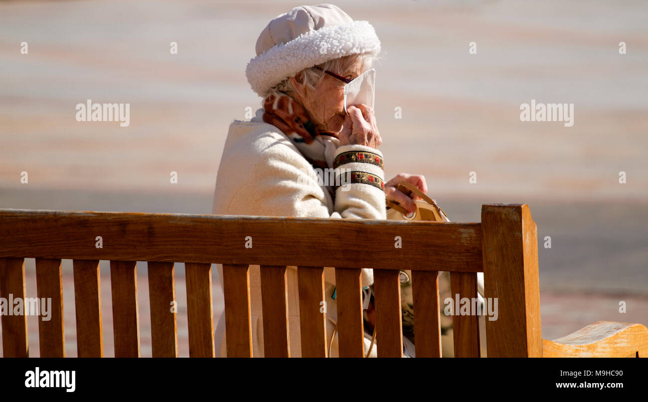 Un quartier chic et femme âgée assise sur un siège de la ville éternuer dans un mouchoir sur une chaude journée de printemps ensoleillée à Dundee, Royaume-Uni Banque D'Images