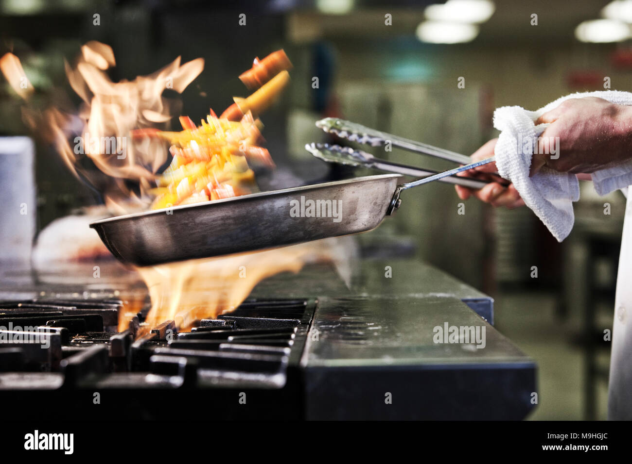 Close-up of chef's hands holding une sauteuse pour cuire les aliments, flambeing contenu. Les flammes s'élevant de la casserole. Banque D'Images