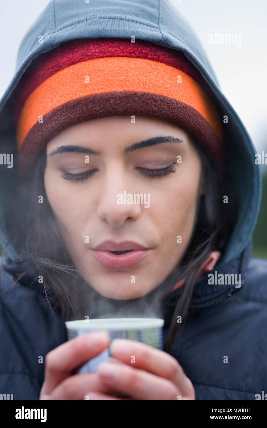 Caucasian woman blowing sur la surface d'une tasse de café chaud sur une journée d'hiver. Banque D'Images