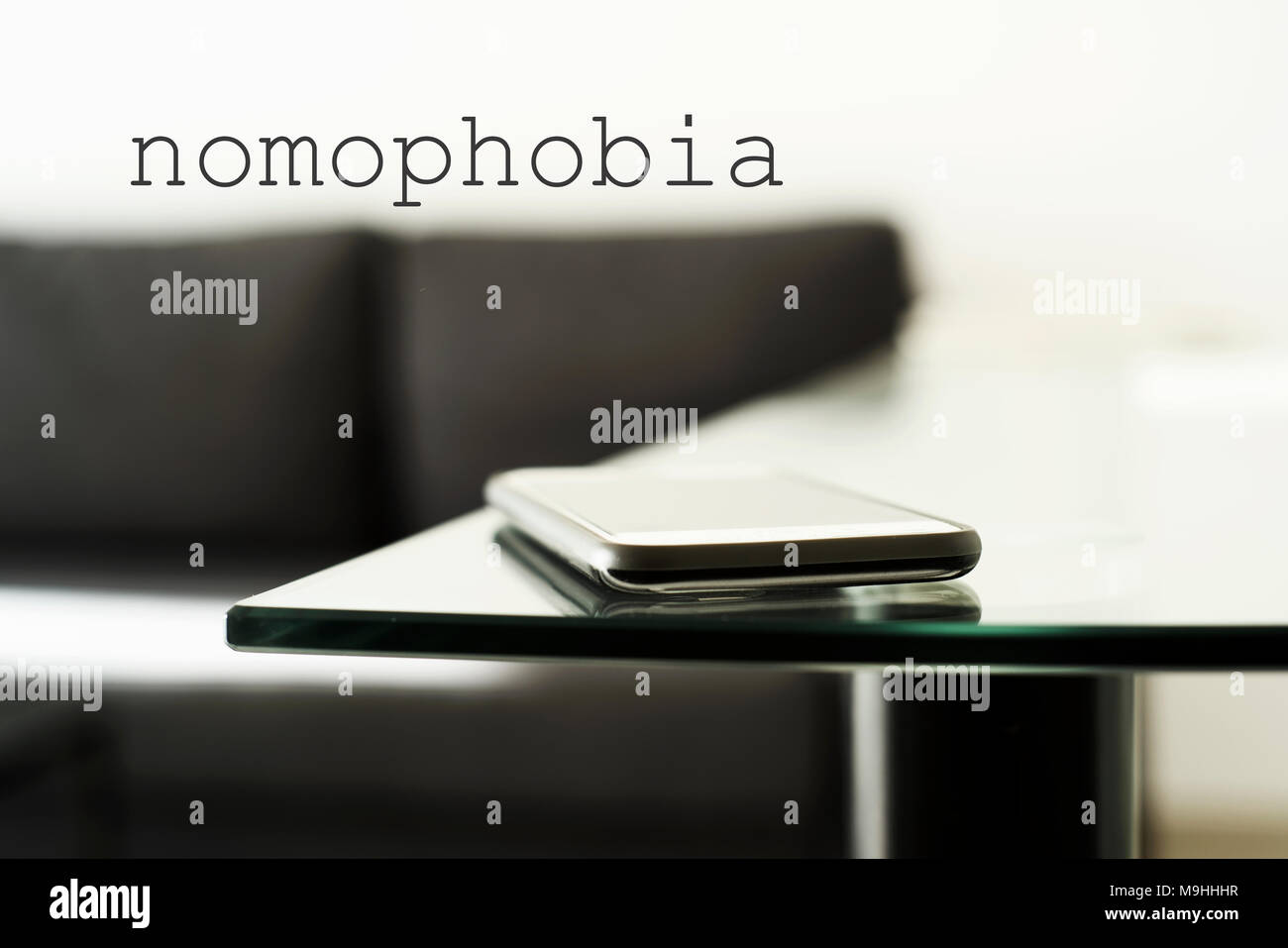 Libre d'un smpartphone sur une table en verre dans un salon moderne ou un hall d'accueil, et le texte nomophobia, pour la phobie de quitter la maison sans le mobi Banque D'Images