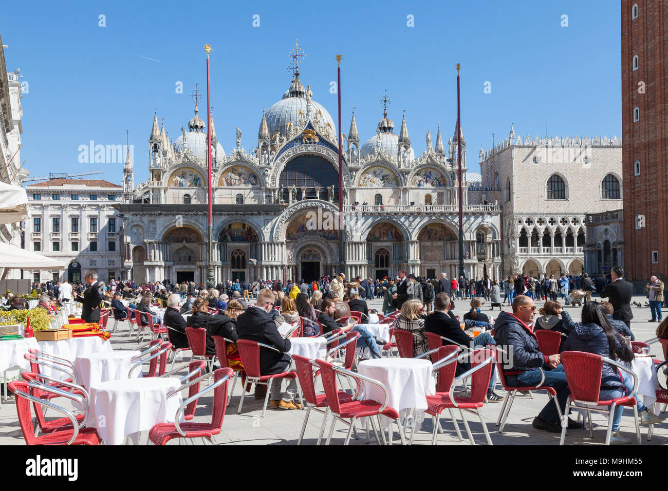 Les gens assis à des tables de restaurant pour le déjeuner sur la Piazza San Marco (Place Saint Marc), Venise, Italie, en face de la Basilique St Marc (basilique San Marco) Banque D'Images