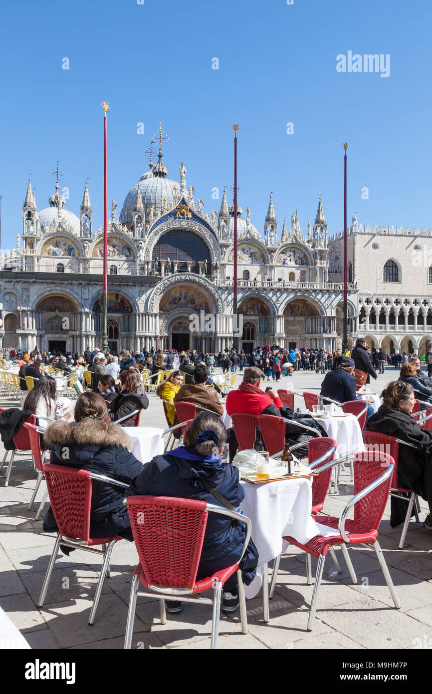 Les gens de prendre un verre au soleil sur la Piazza San Marco (Place Saint Marc), Venise, Vénétie, Italie, en face de la Basilique de San Marco (Basilique St Marc) Banque D'Images