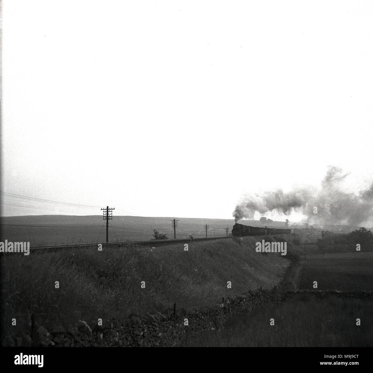 Années 1950, historiques, une distance photo d'une locomotive à vapeur et de wagons de train sur une ligne de chemin de fer en milieu rural mis en banque, England, UK. Banque D'Images