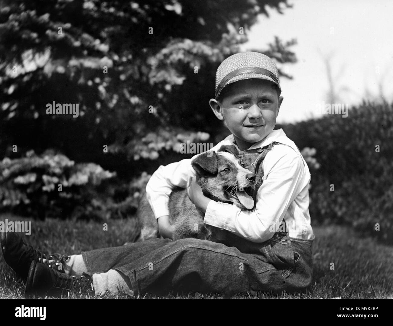 Un jeune garçon embrasse son chien, ca. 1920. Banque D'Images