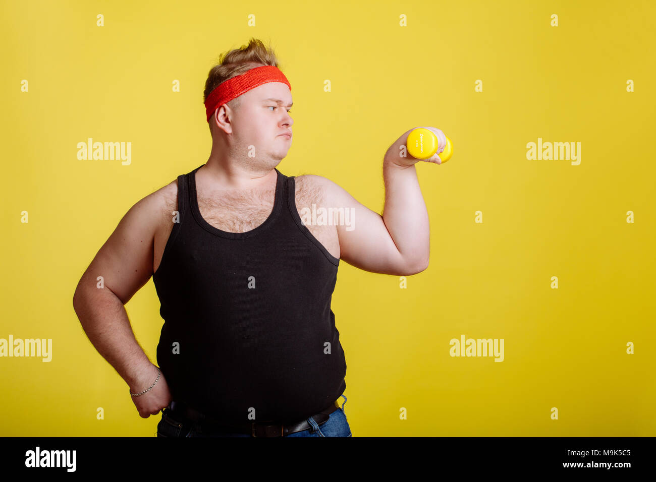 Gros homme épais avec haltère sur fond jaune. Motivation pour les personnes  grosses. chemise noire, gros ventre, bandeau rouge Photo Stock - Alamy