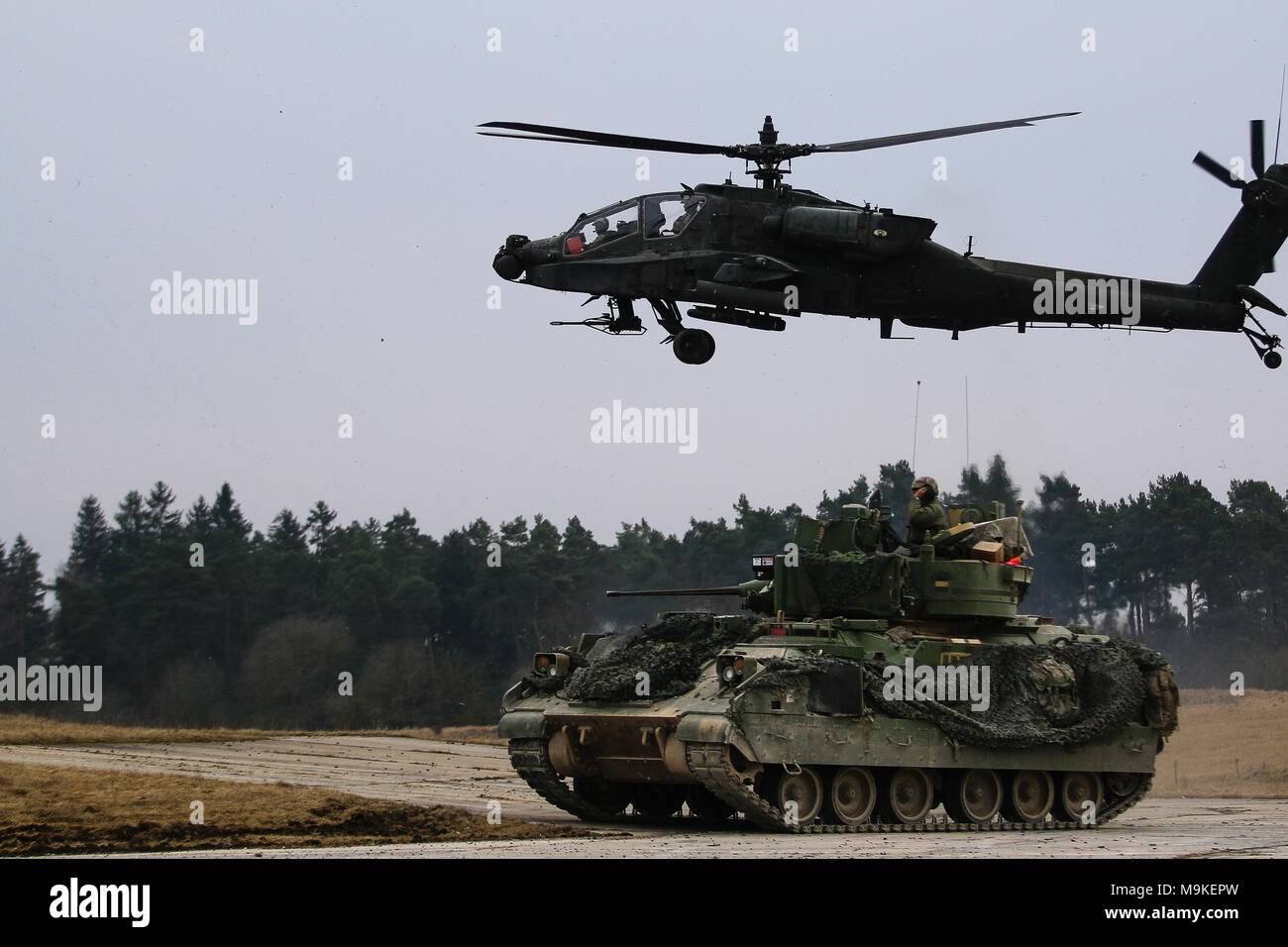 L'armée américaine d'un véhicule de combat Bradley M2 de 5e Escadron, 4e régiment de cavalerie blindée, 2e Brigade Combat Team, 1re Division d'infanterie et un hélicoptère Apache AH-64 avec 1er Bataillon, 3e Régiment d'aviation, 12e Brigade d'aviation de combat, sécuriser une zone au cours d'un exercice de tir réel interarmes (CALFEX) dans la zone d'entraînement Grafenwoehr, Allemagne, Mar 26, 2018. (U.S. Photo de l'armée par la CPS. Hubert D. Delany III / 22e Détachement des affaires publiques mobiles) Banque D'Images