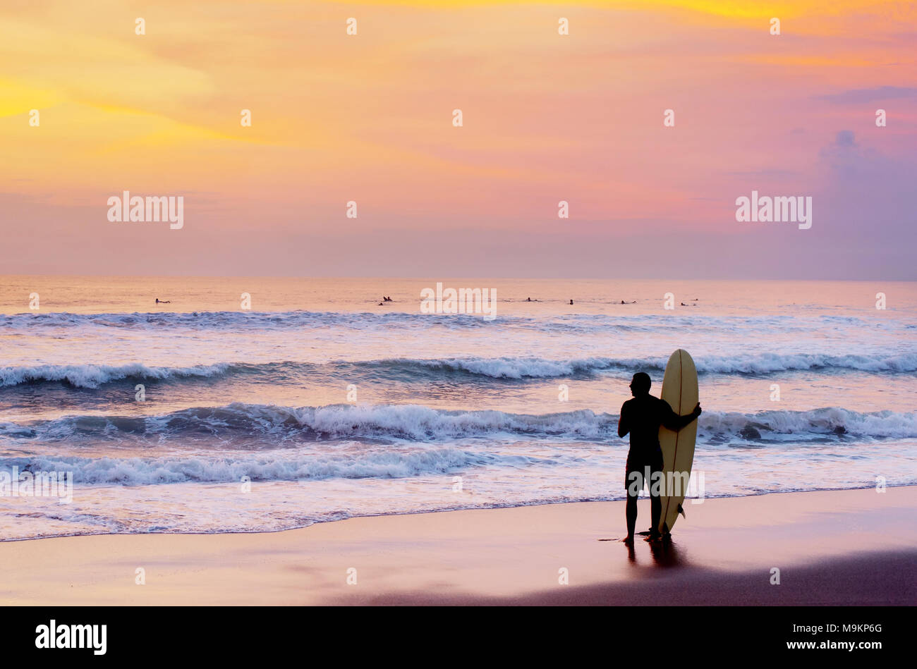 Surfer à la plage avec une planche de surf au coucher du soleil. L'île de Bali, Indonésie Banque D'Images