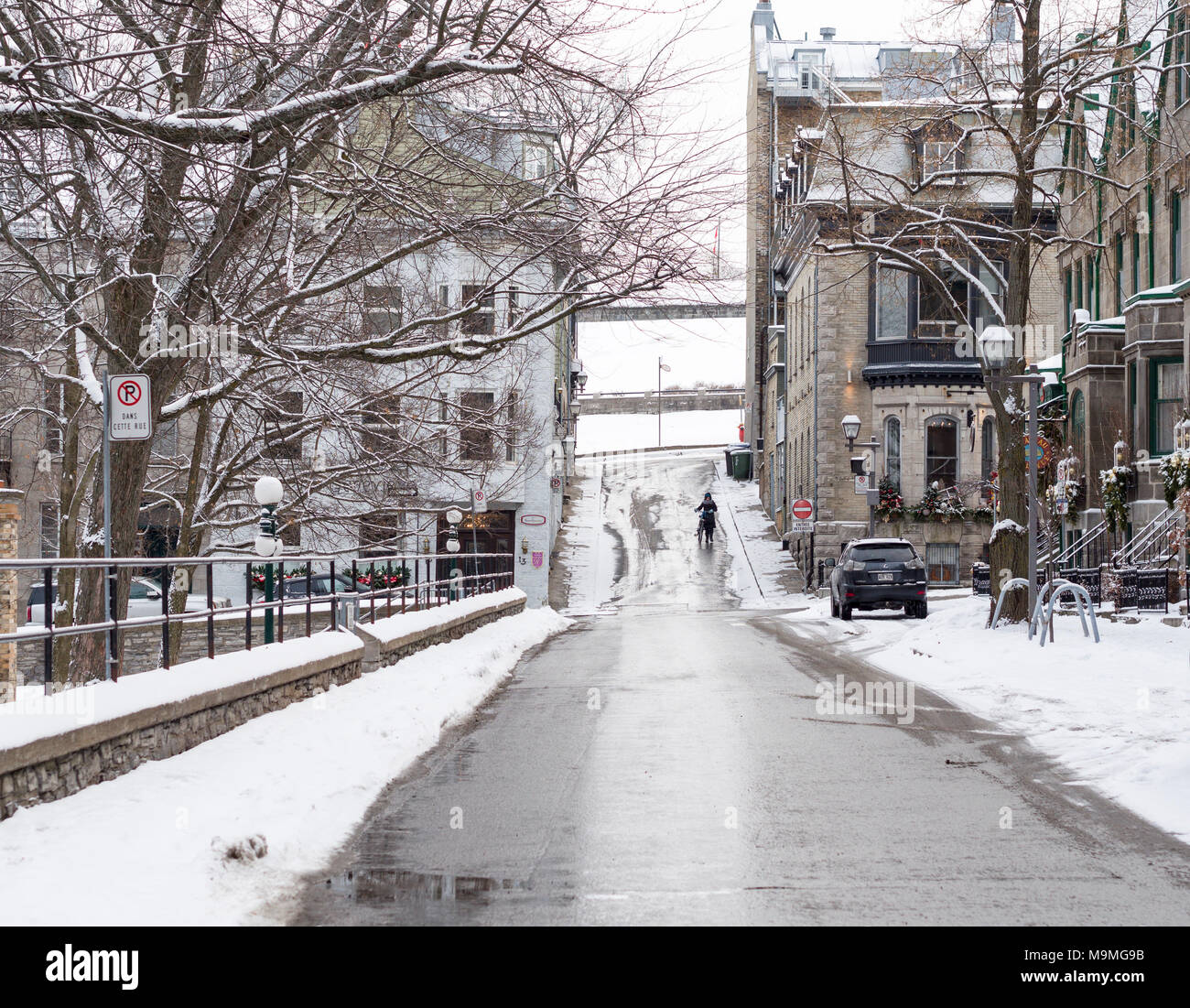 Femme avec vélo sur le Vieux Québec street en hiver : une femme entre son vélo dans une rue en pente, la neige dans le Vieux Québec près de la citadelle. Banque D'Images