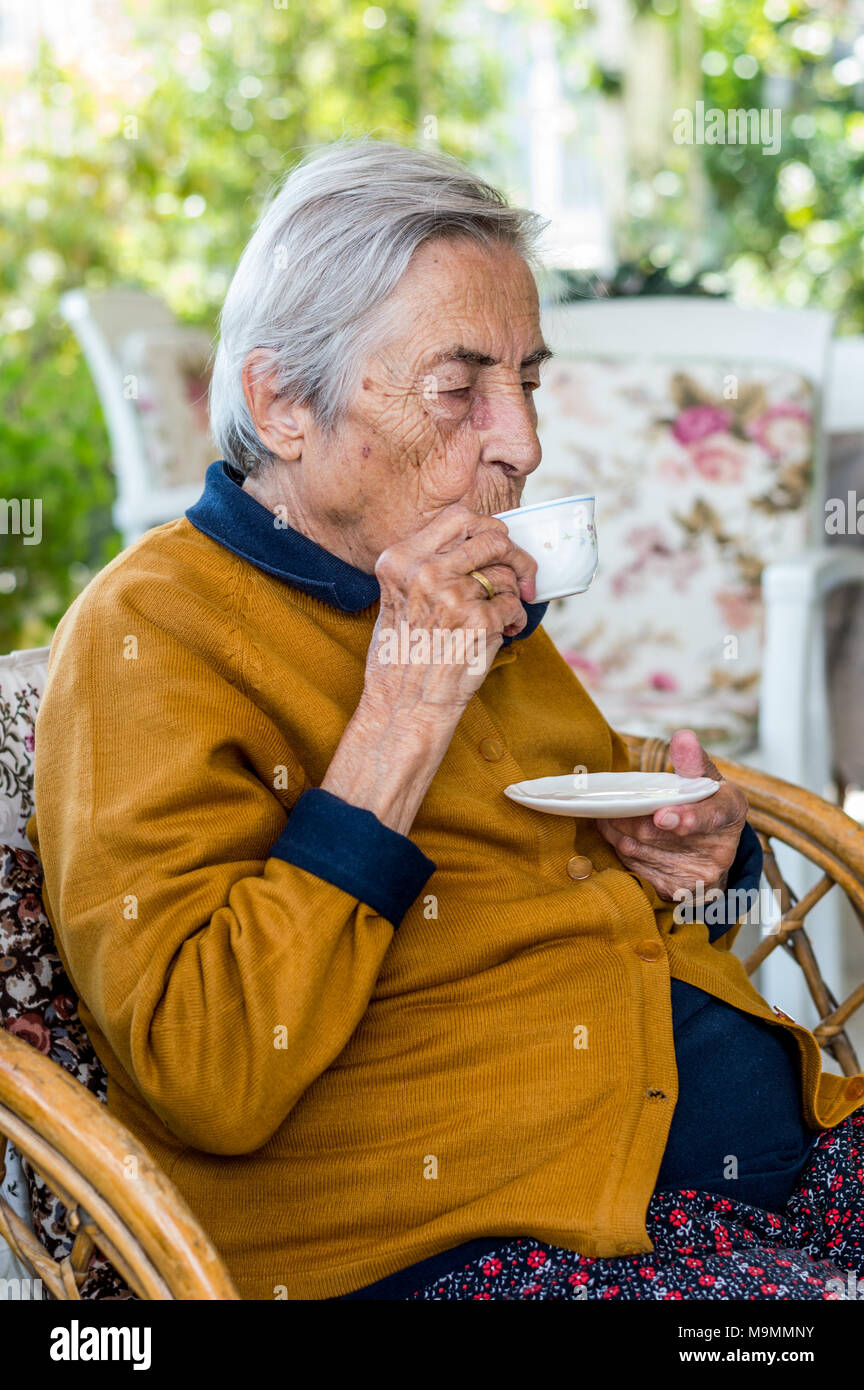 Femme âgée assis et boire le café turc dans le balcon sur une journée ensoleillée. Banque D'Images