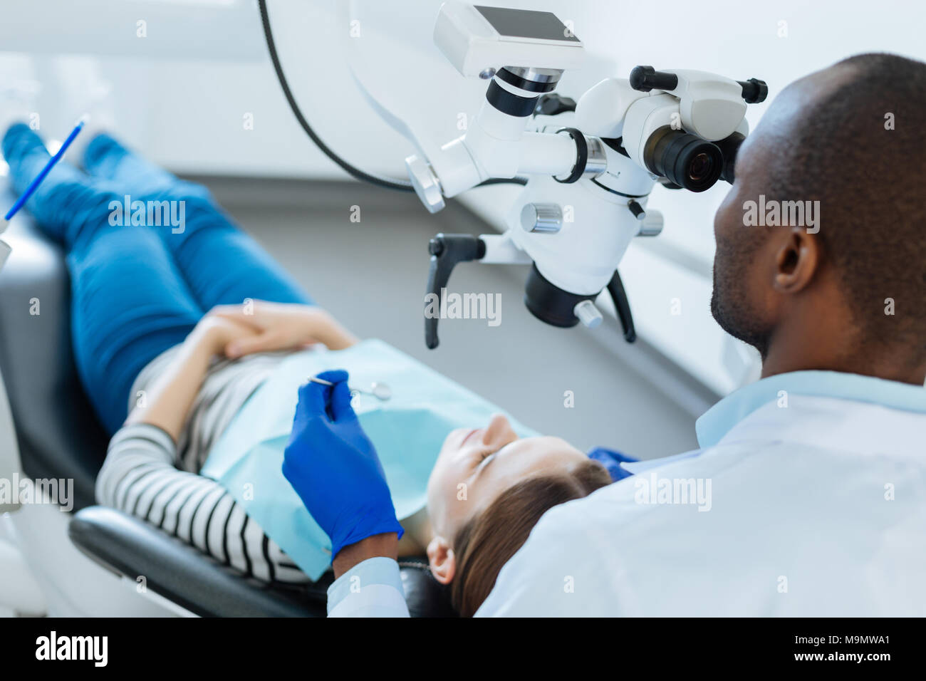 Mesure nécessaire. Qualifiés agréable contrôle dentiste dents de ses patients pour les micro-fissures à l'aide d'un microscope pendant qu'elle couchée dans le dentiste Banque D'Images