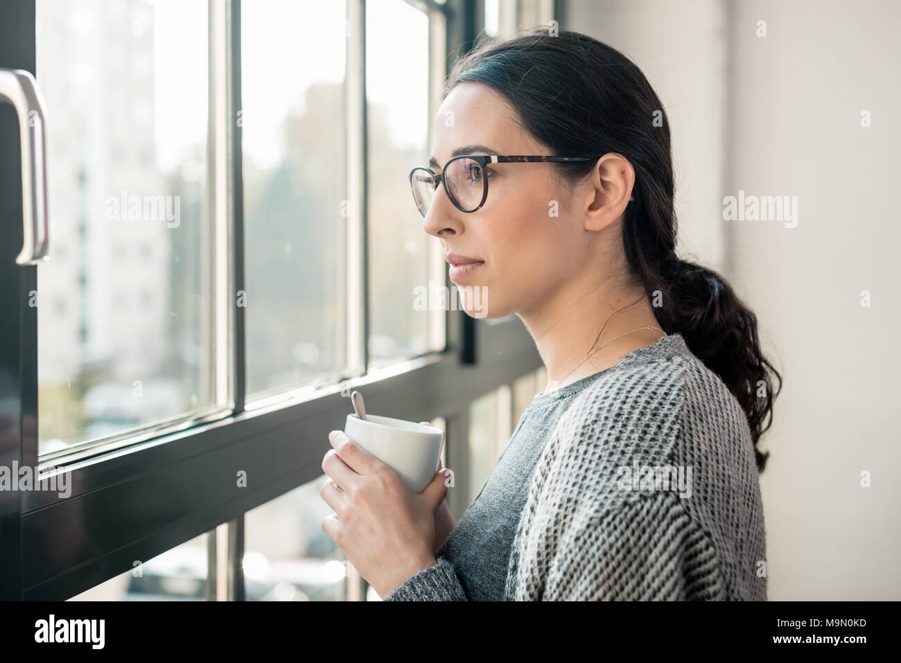 Jeune femme pensive en regardant par la fenêtre pendant les pauses Banque D'Images