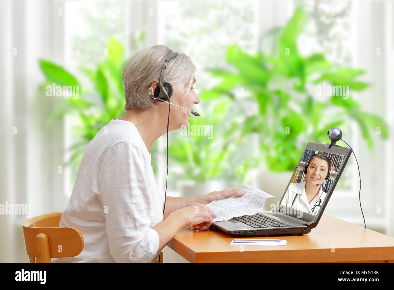 Senior woman sitting at a table dans sa salle de séjour avec la notice de son médicament prescrit pendant un appel vidéo avec son médecin Banque D'Images