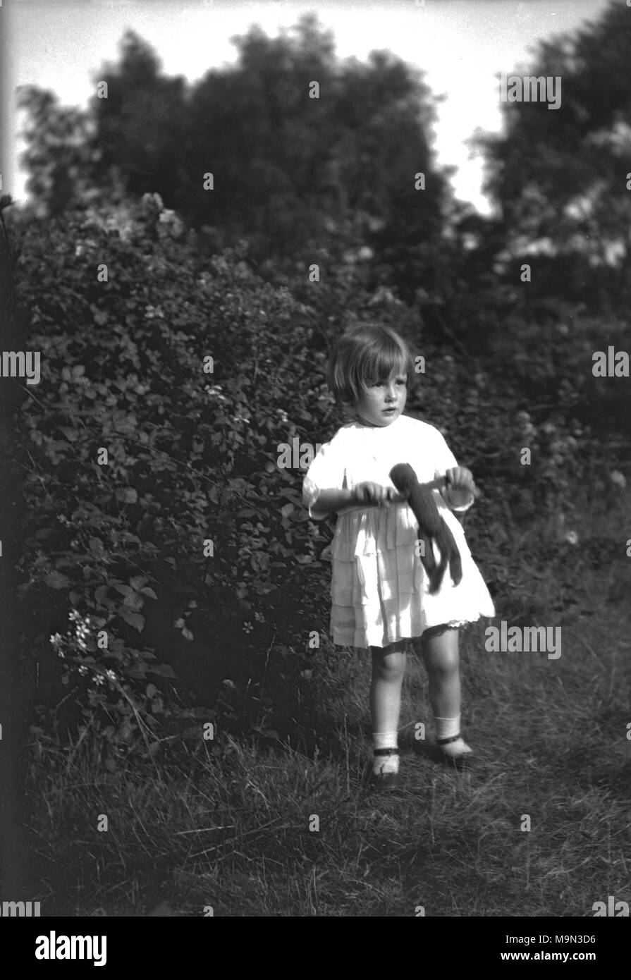 Années 1930, historiques, jeune fille à l'extérieur dans un jardin tenant son petit doudou consolateur, un ours en peluche, England, UK. Banque D'Images