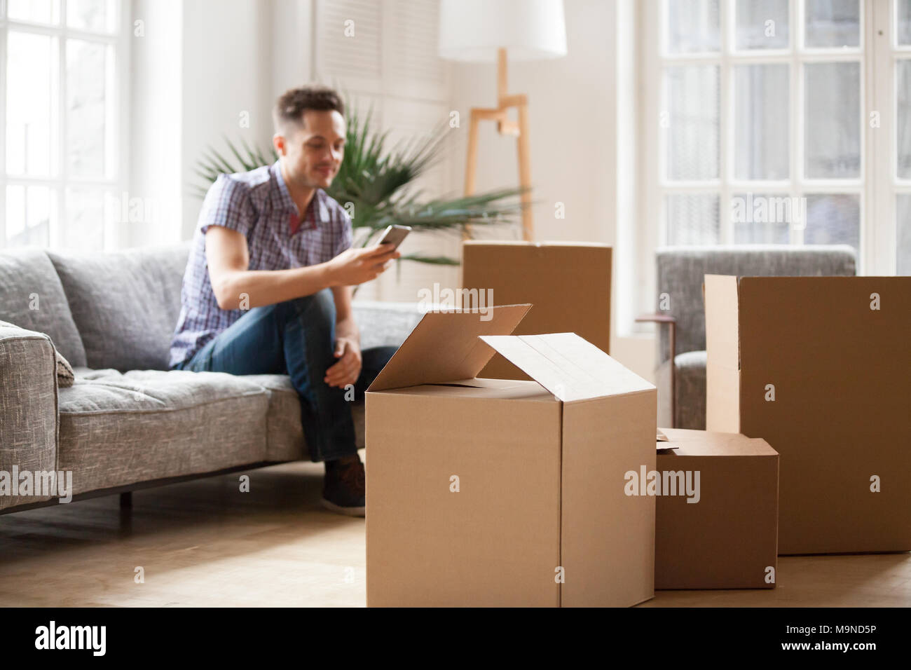 Paniers boîtes en carton avec young man sitting on sofa in living room service appelant à l'arrière-plan, effets personnels en carton en attente f Banque D'Images