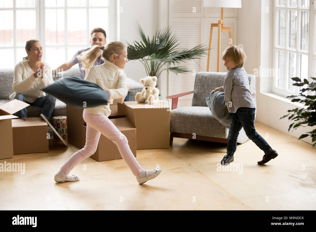 Heureux les enfants actifs body glamour le jour du déménagement, happy girl and boy playing ensemble dans nouvelle maison alors que les parents des enfants rire, fam Banque D'Images