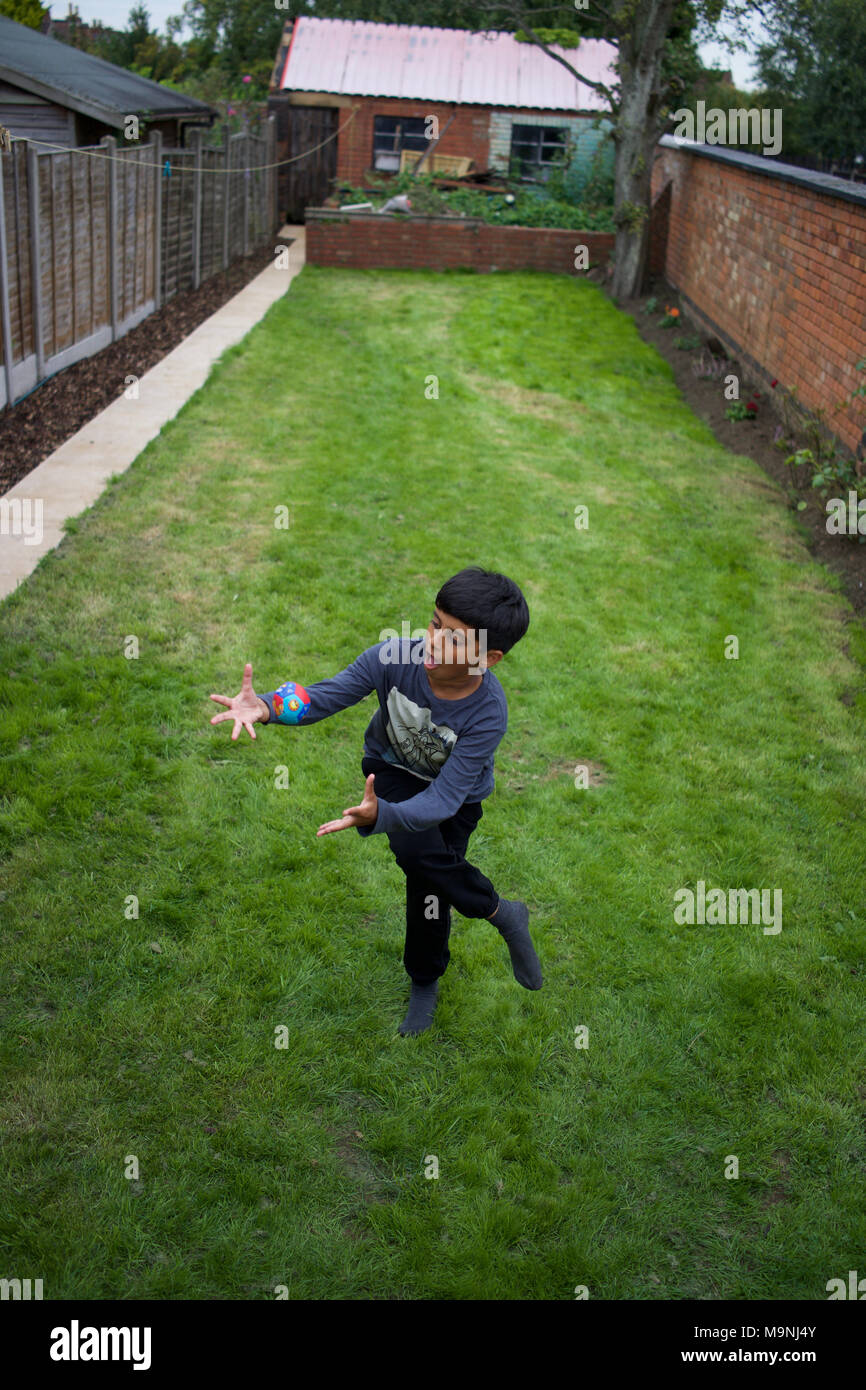 Garçon pakistanais jouant avec une balle dans l'arrière-jardin, Rugby, Angleterre Banque D'Images