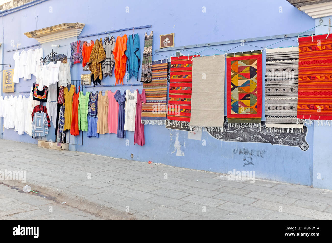 Les vêtements et les tapis sont exposés à la vente le long d'un mur dans le centre historique de Oaxaca, Mexique. Banque D'Images