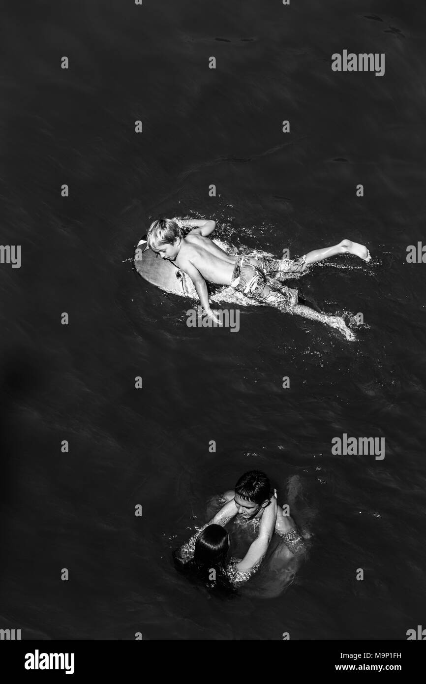 Regarder sur young man and woman embracing dans l'eau tandis qu'un jeune garçon a proximité flottant sur l'air. La Fédération, la rivière Monte Rio, en Californie. Banque D'Images