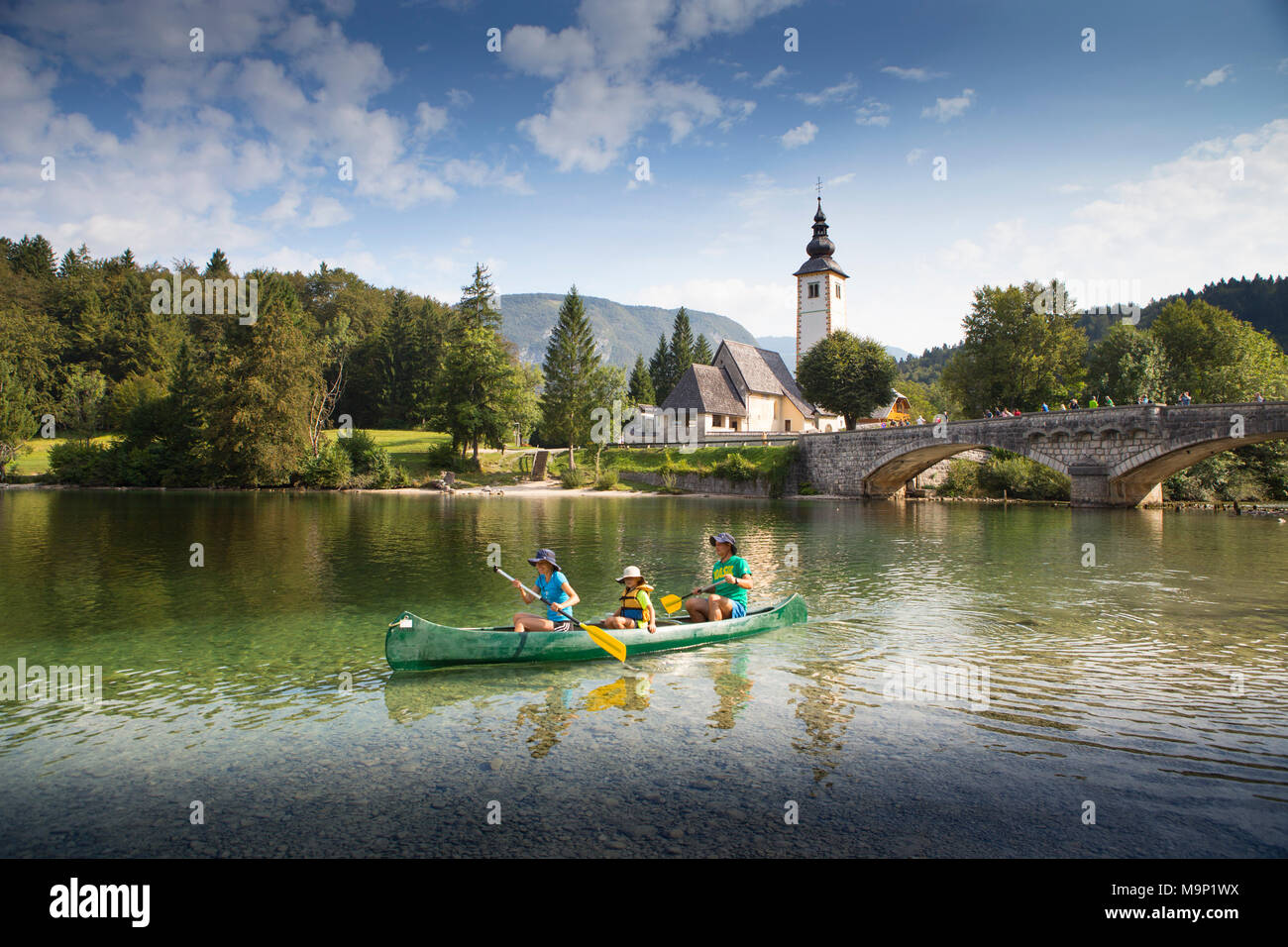 Famille en canoë sur le lac de Bohinj, avec l'église et pont de Ribcev Laz en arrière-plan, Triglav, Slovénie Banque D'Images