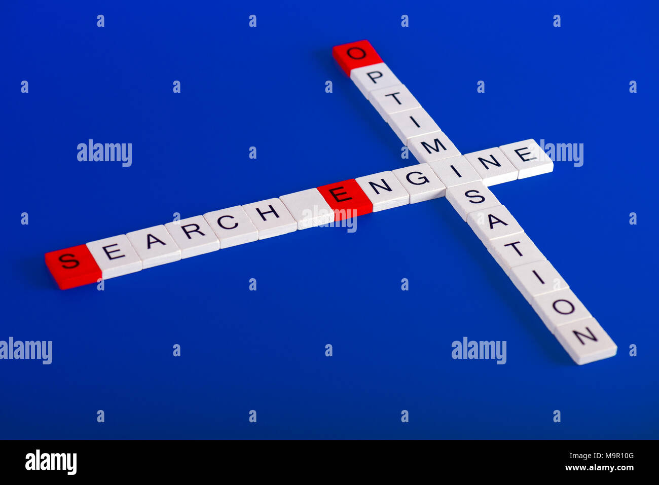 L'optimisation de Search Engine (SEO) faite de blocs en bois blanc sur fond bleu dans le style de mots croisés, les premières lettres sont rouges Banque D'Images