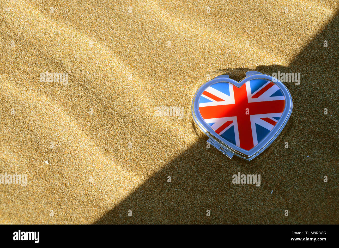 Une Union jack le couvert d'un étain en forme de cœur allongé sur une plage de sable. Banque D'Images