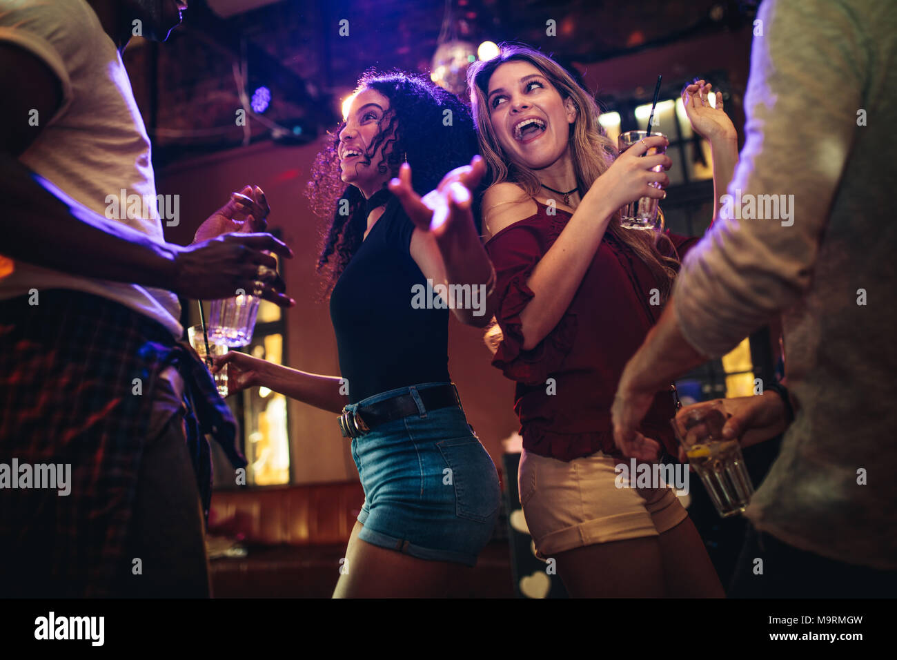 Heureux les jeunes femmes danser et faire la fête avec des amis à la discothèque. Groupe d'amis profitant à bar avec boissons. Banque D'Images