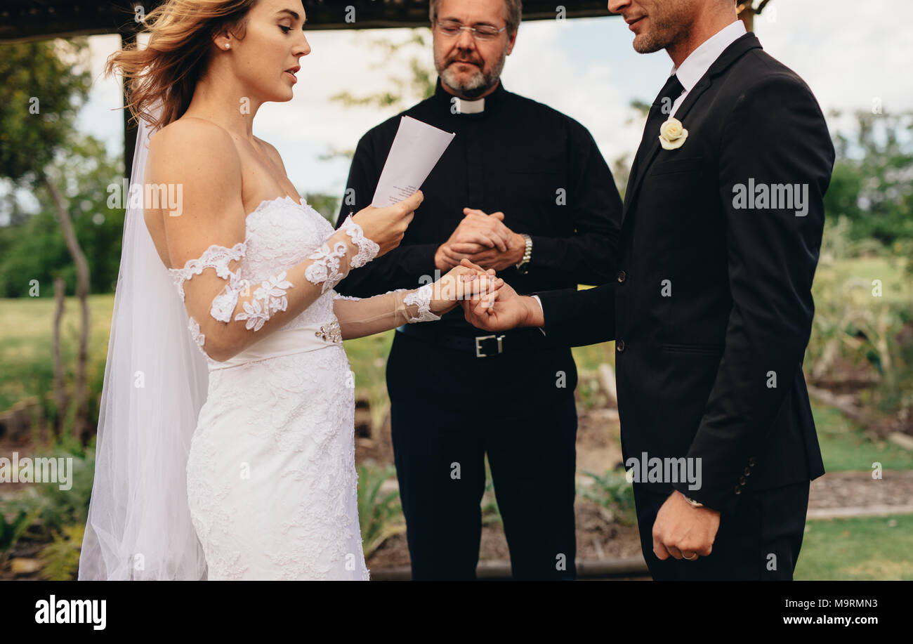 Bride holding un papier et la lecture des vœux de mariage, avec le ministre debout dans l'arrière-plan. L'échange de quelques vœux lors de la cérémonie du mariage. Banque D'Images Bride holding un papier et la lecture des vœux de mariage, avec le ministre debout dans l'arrière-plan. L'échange de quelques vœux lors de la cérémonie du mariage. Banque D'Images
