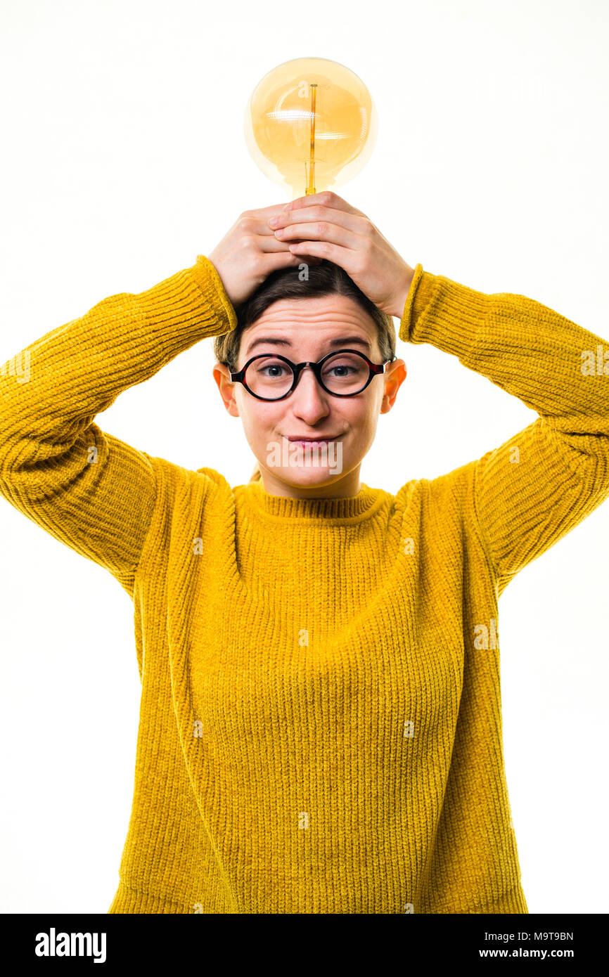 L'inspiration et de la créativité - le moment d'ampoule : un jeune 'lol' à la race blanche femme fille portant un chandail et cavalier jaune lunettes rondes, tenant un vieux rétro-style ampoule elecric , sur un fond blanc, UK Banque D'Images