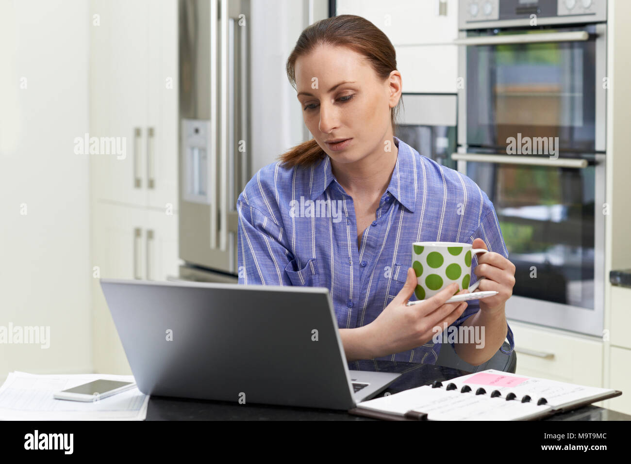Offres et demandes de missions femme Worker Using Laptop et boire du café dans la cuisine à la maison Banque D'Images