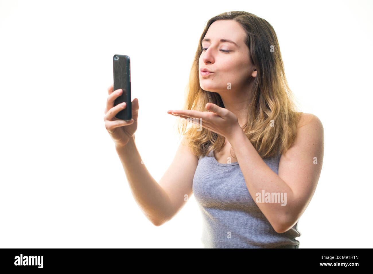 Une jeune femme de race blanche girl blowing a kiss et prendre une photographie à l'aide d'un iPhone selfies cell phone téléphone mobile , d'afficher sur son instagram snapchat et autres médias sociaux - UK Banque D'Images