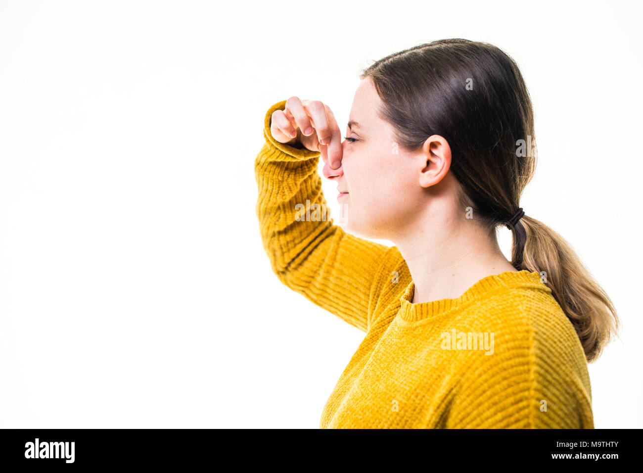 Une jeune femme de race blanche fille portant un chandail de cavalier jaune, de pincement ou de tenir son nez pour bloquer un stinky malodorantes terrible, de l'environnement nuisibles , debout sur un fond blanc, UK Banque D'Images