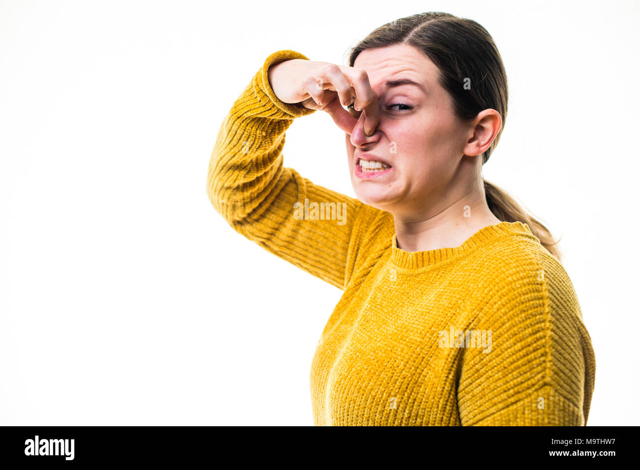 Une jeune femme de race blanche fille portant un chandail de cavalier jaune, de pincement ou de tenir son nez pour bloquer un stinky malodorantes terrible, de l'environnement nuisibles , debout sur un fond blanc, UK Banque D'Images