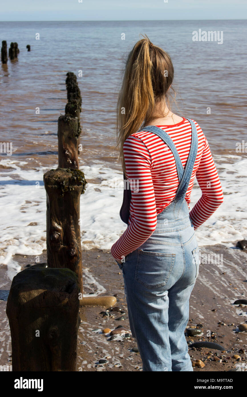 Teenage girl looking out jusqu'à la mer en salopette en jean et une bande  rouge en haut, rejette point, Yorkshire, UK Photo Stock - Alamy