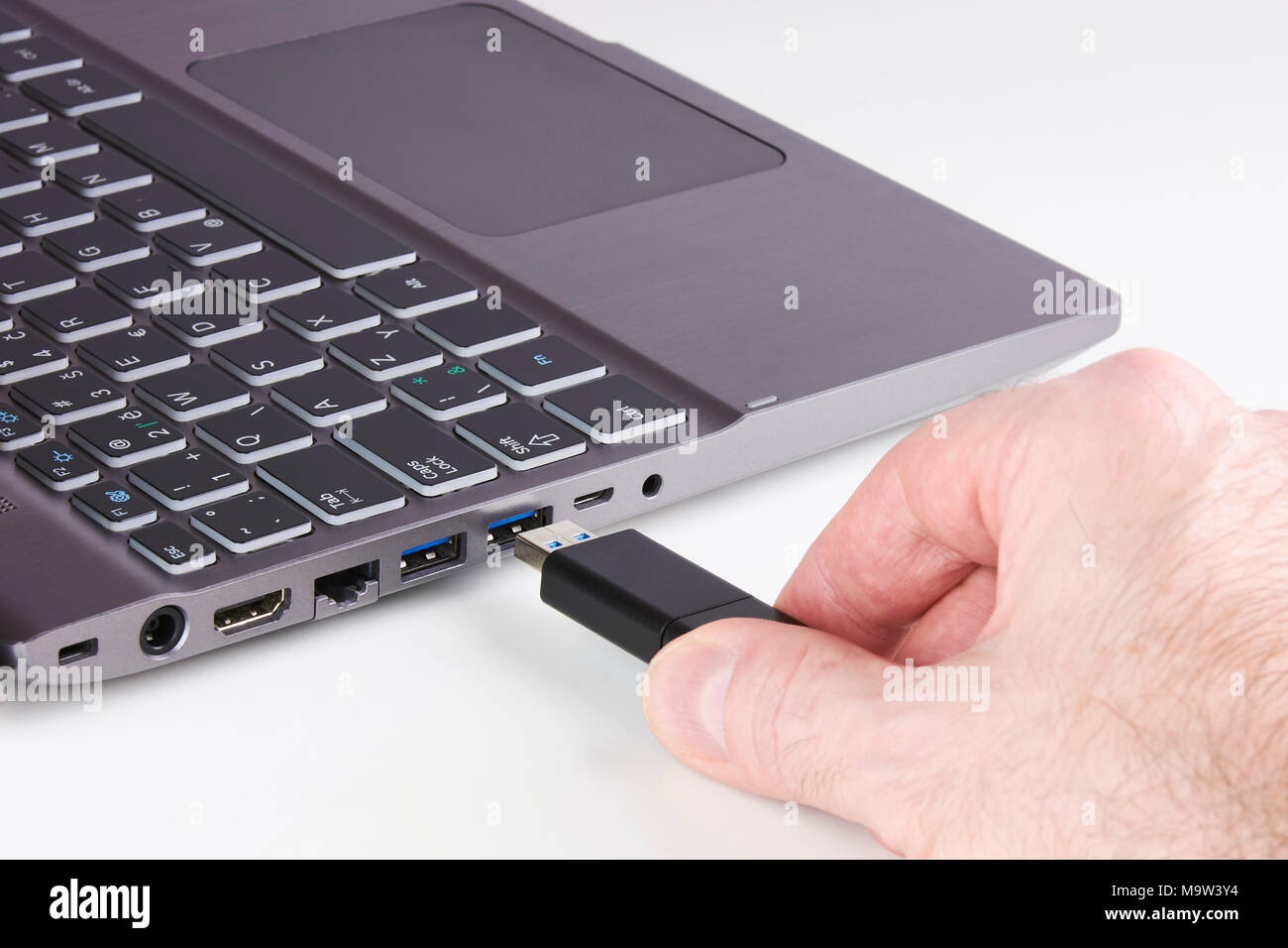 Ordinateur portable d'argent et de sexe masculin hand holding disque Flash USB et le brancher dans l'emplacement - sur fond blanc Banque D'Images