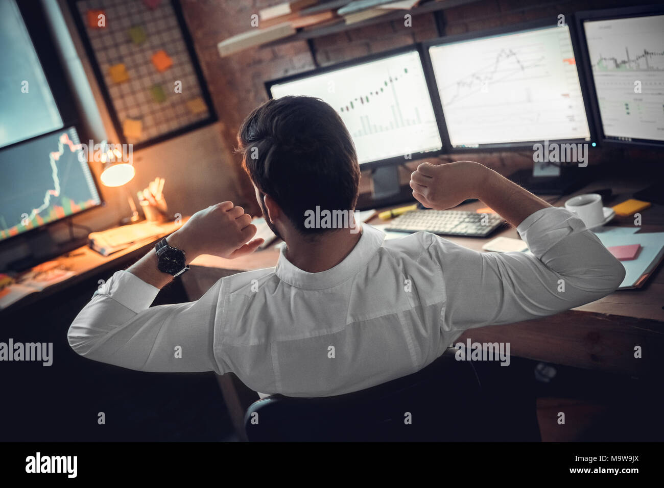 Vue arrière au courtier stock trader ou l'investisseur qui s'étend les mains au travail fatigué après de longues à l'aide d'ordinateur, de l'homme d'affaires travail fini de prendre de pause pour Banque D'Images