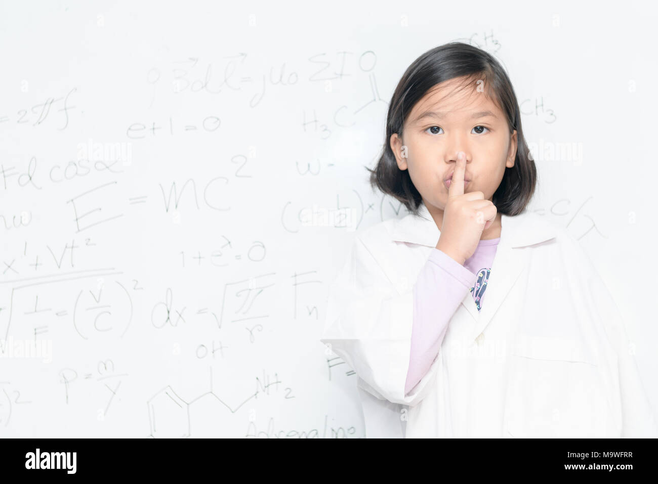 Fille scientifique disant hush être calme avec un doigt sur les lèvres geste sur inscription blanche avec l'équation scientifique, de la science et de l'éducation préscolaire concept Banque D'Images