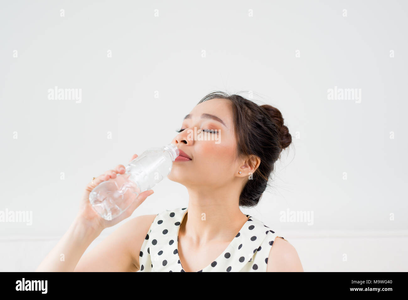 Belle jeune femme asiatique tenant un verre d'eau tout en restant assis à la maison Banque D'Images