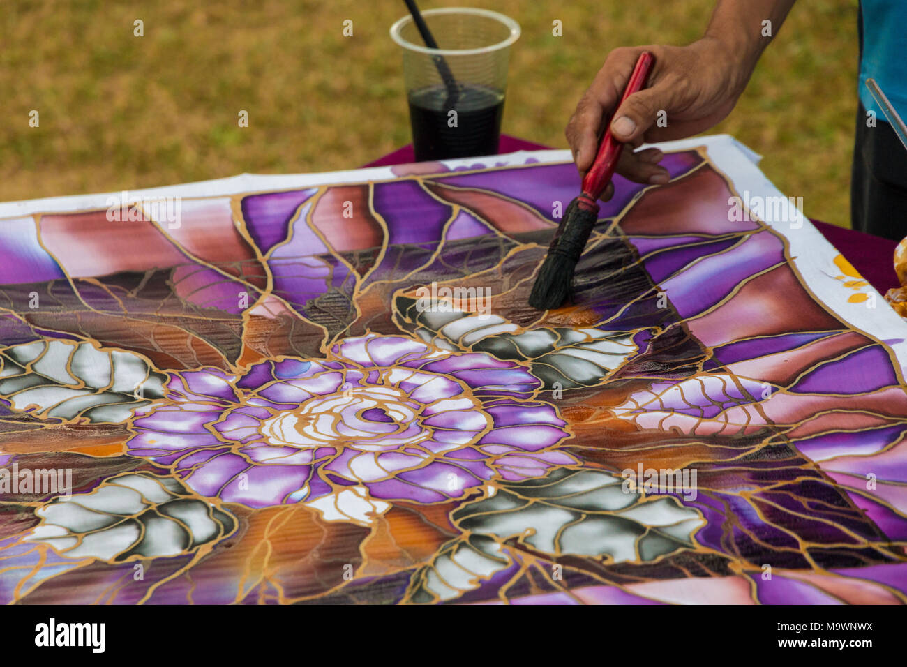 Portrait d'un artisan batik malaisien montrant comment brosser sur les couleurs de peinture d'un tissu à motif populaire de feuilles et de fleurs. Banque D'Images