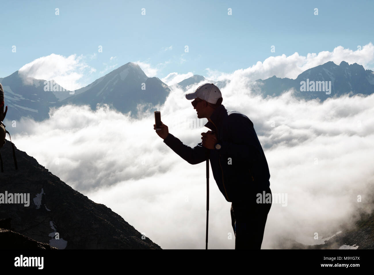 Hipster homme tire une vidéo d'un paysage de montagne avec des nuages sur un téléphone mobile, alors que l'article de fond contre les hauts sommets. L'homme est tak Banque D'Images